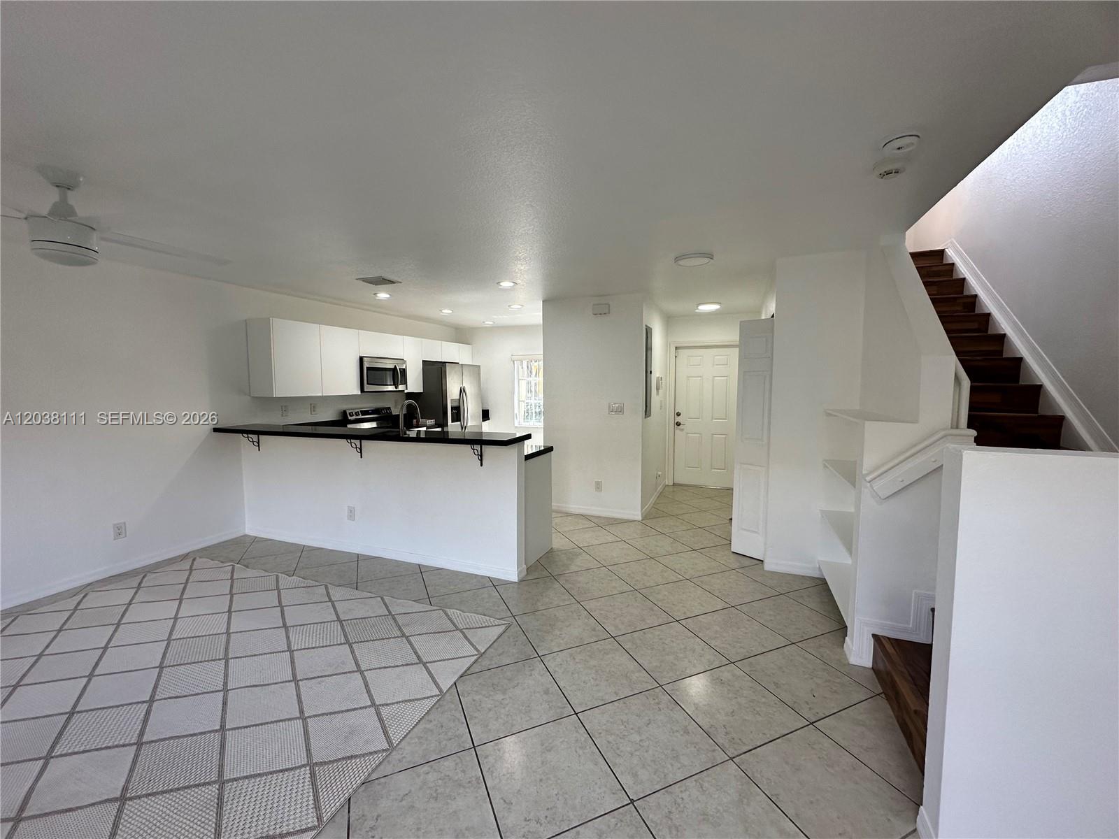 An open-concept kitchen with white cabinets and a breakfast bar overlooks a tiled living area — 324 NE 3rd St # D, Hallandale Beach FL 33009, HALLANDALE BEACH, FL