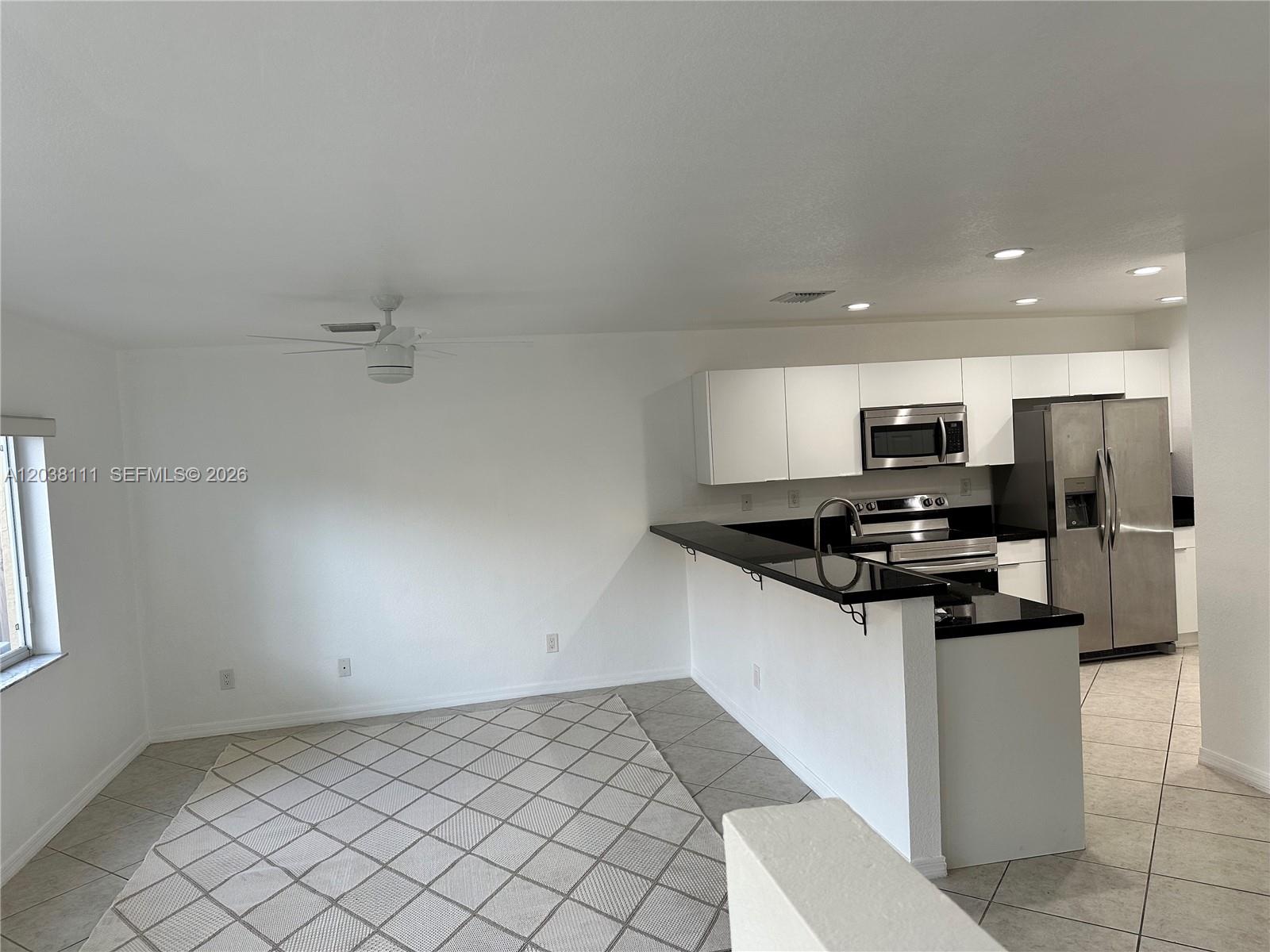 A kitchen with black countertops and white cabinets opens to a tiled dining area — 324 NE 3rd St # D, Hallandale Beach FL 33009, HALLANDALE BEACH, FL