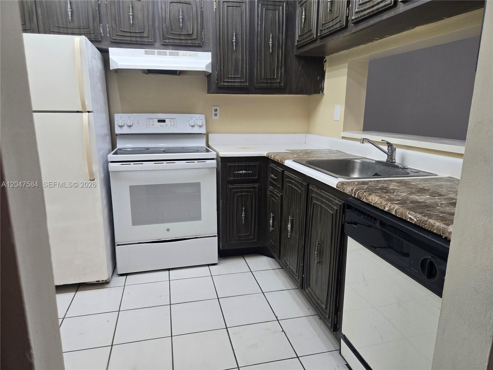 A kitchen features dark wood cabinets, white appliances, a marble-patterned countertop, and white tile flooring — 482 NW 165th St Rd # 505, Miami FL 33169, MIAMI, FL