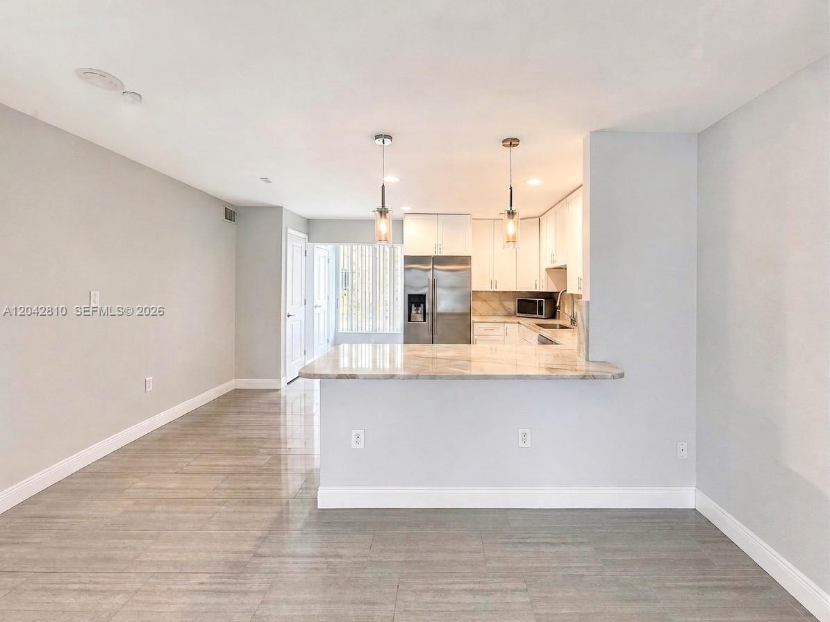 A kitchen with white cabinets and a marble-topped breakfast bar overlooks a tiled room — NAPLES, FL