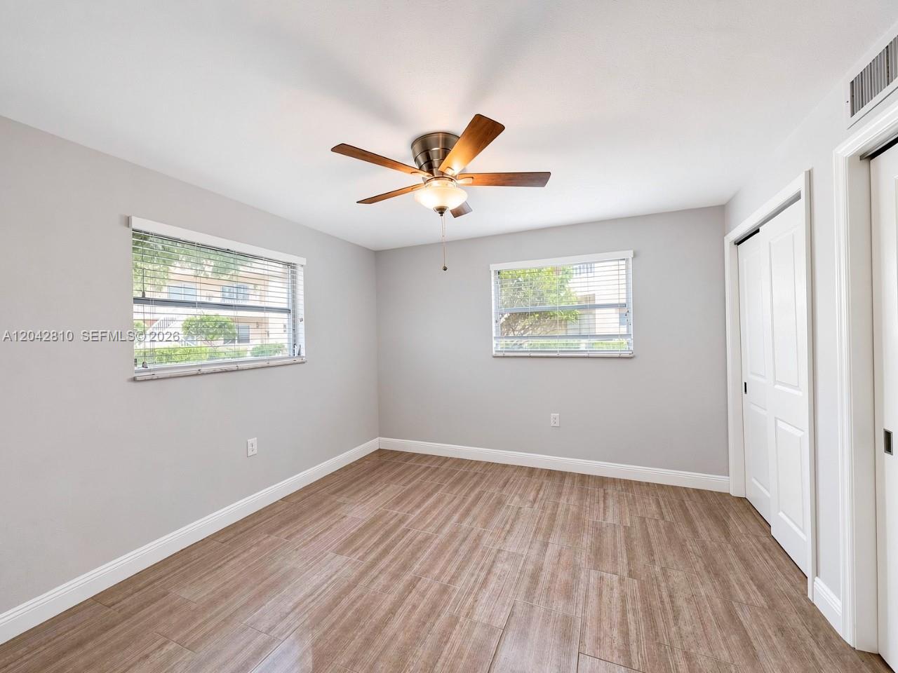 A bedroom features light gray walls, wood-look tile flooring, a ceiling fan, and two windows — NAPLES, FL