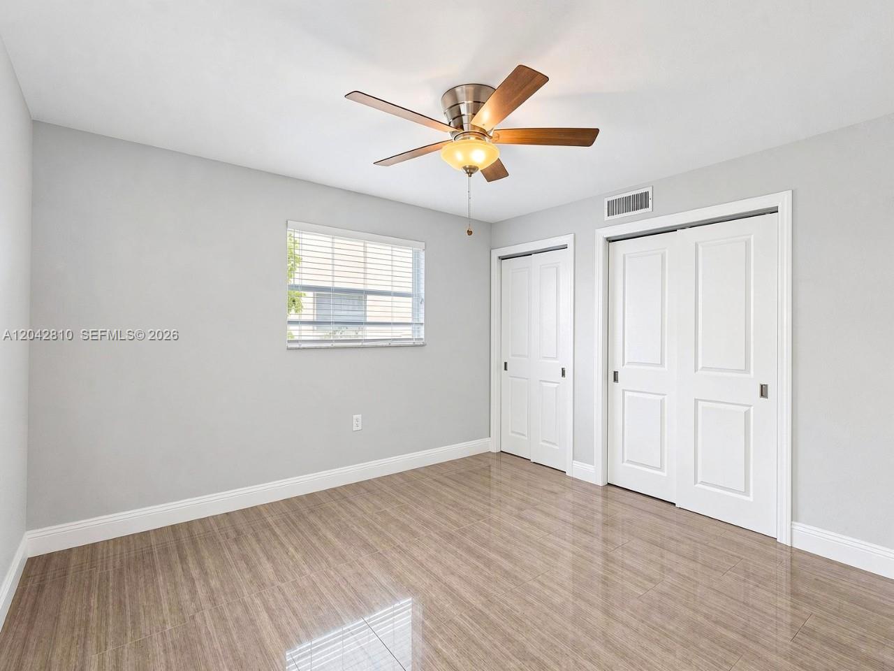 A bedroom features light gray walls, wood-look tile flooring, a ceiling fan, and two closets — NAPLES, FL