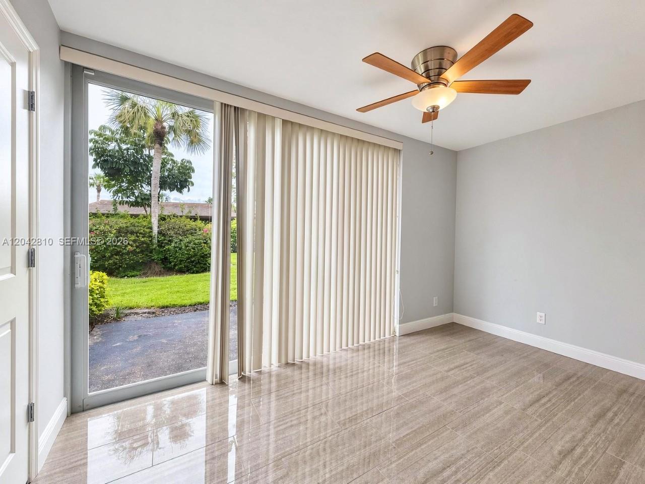 A room with light gray walls, tile flooring, a ceiling fan, and sliding glass doors — NAPLES, FL