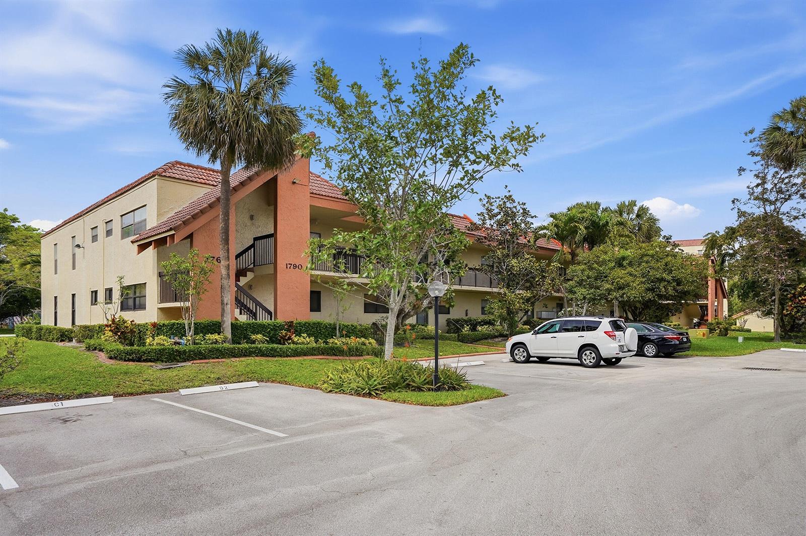 A multi-story apartment building with a tan facade and orange accents sits behind a parking lot — 1774 Hammock Boulevard # 118, Coconut Creek FL 33063, COCONUT CREEK, FL