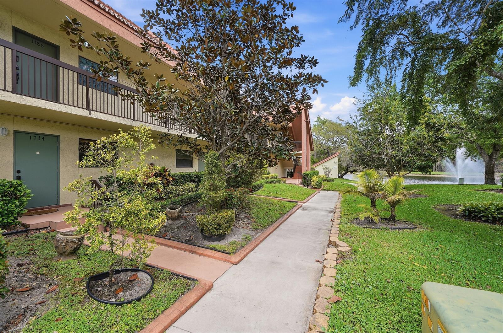 A two-story apartment building exterior features a concrete walkway, landscaping, and a fountain in back — 1774 Hammock Boulevard # 118, Coconut Creek FL 33063, COCONUT CREEK, FL