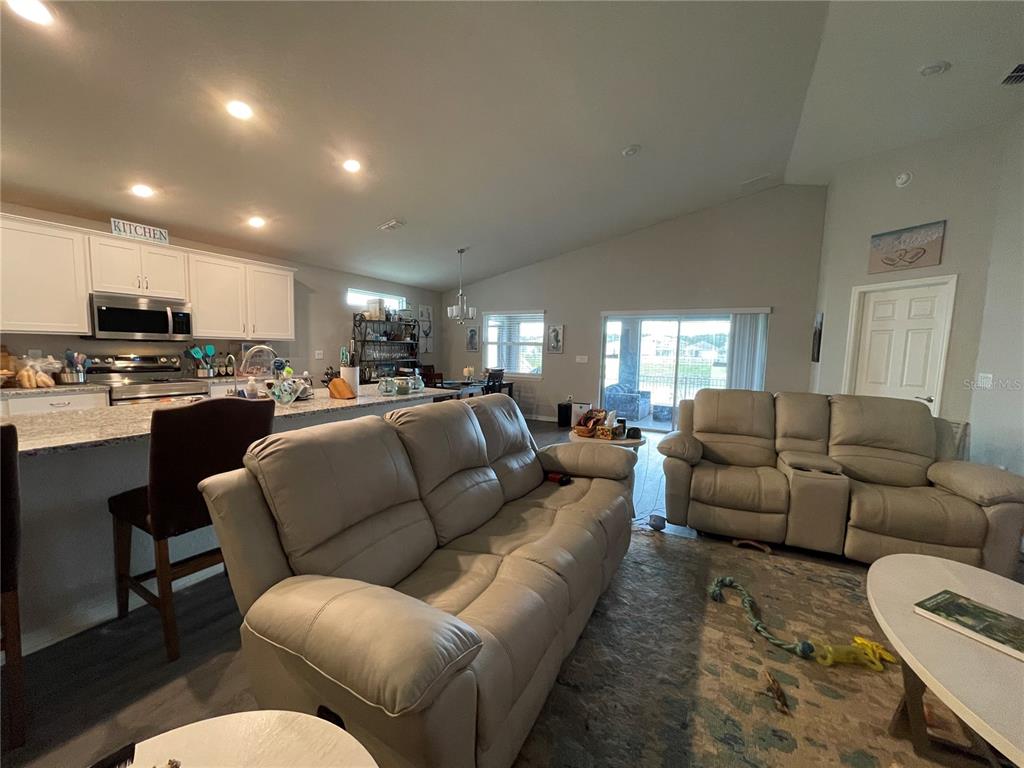 An open-concept living room features light-colored leather sofas, a kitchen island, and sliding glass doors — 2824 SAN MARCO WAY, WINTER HAVEN, FL
