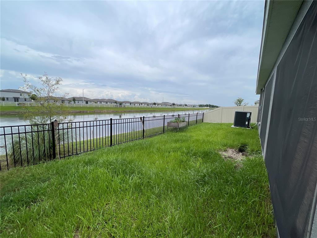 A grassy backyard features a black metal fence overlooking a pond under a cloudy sky — 2824 SAN MARCO WAY, WINTER HAVEN, FL