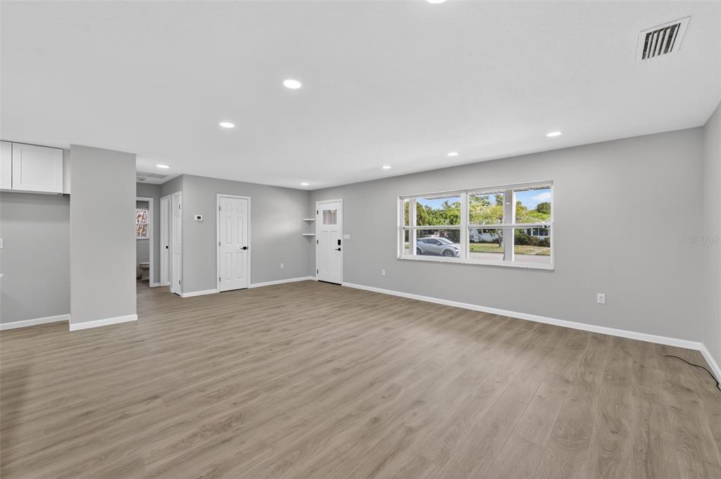 An empty living room with light gray walls, wood-look flooring, recessed lighting, and a front door — 6224 7TH AVENUE DRIVE W, BRADENTON, FL