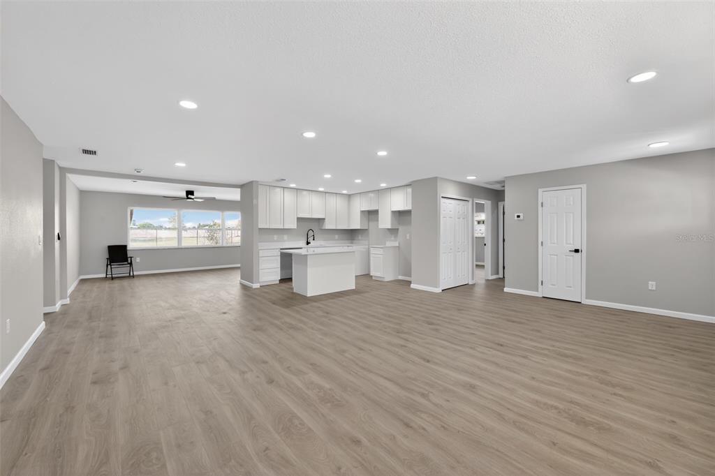 An open-concept living area features light wood-look flooring, white kitchen cabinetry, and recessed lighting — 6224 7TH AVENUE DRIVE W, BRADENTON, FL