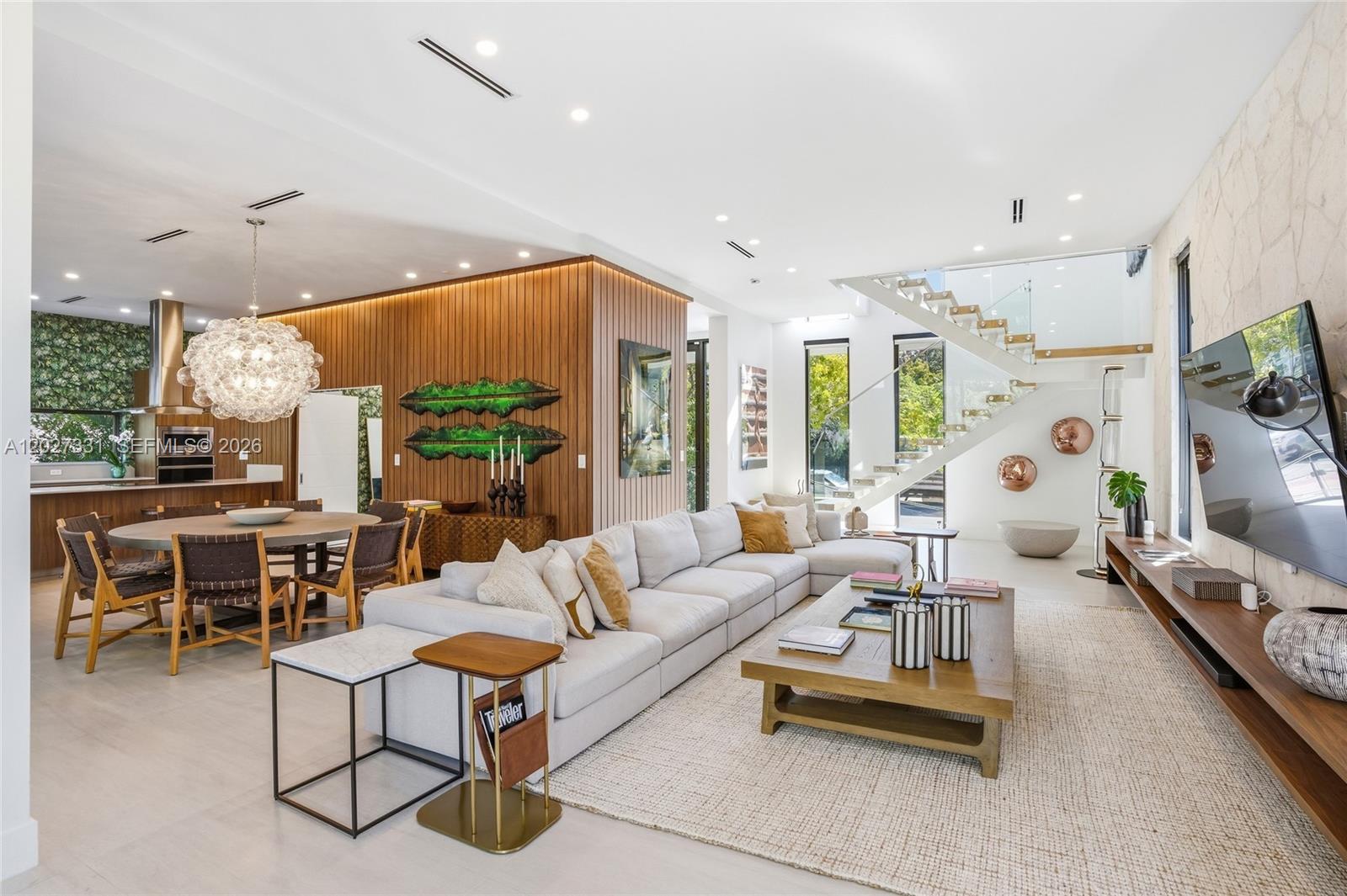A modern open-concept living and dining area features a large sectional sofa and wooden staircase — 4354 Alton Rd, Miami Beach FL 33140, MIAMI BEACH, FL
