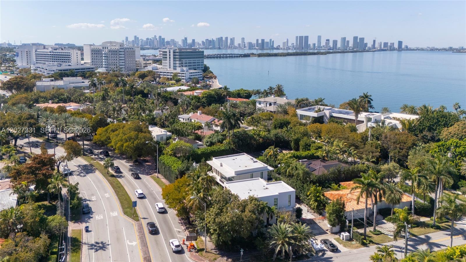 An aerial view shows a coastal neighborhood with lush trees, modern houses, and a city skyline — 4354 Alton Rd, Miami Beach FL 33140, MIAMI BEACH, FL
