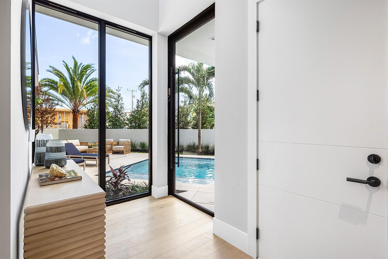 A bright entryway features a light wood console, white door, and glass walls overlooking a pool — 810 Andrews Avenue, Delray Beach FL 33483, DELRAY BEACH, FL