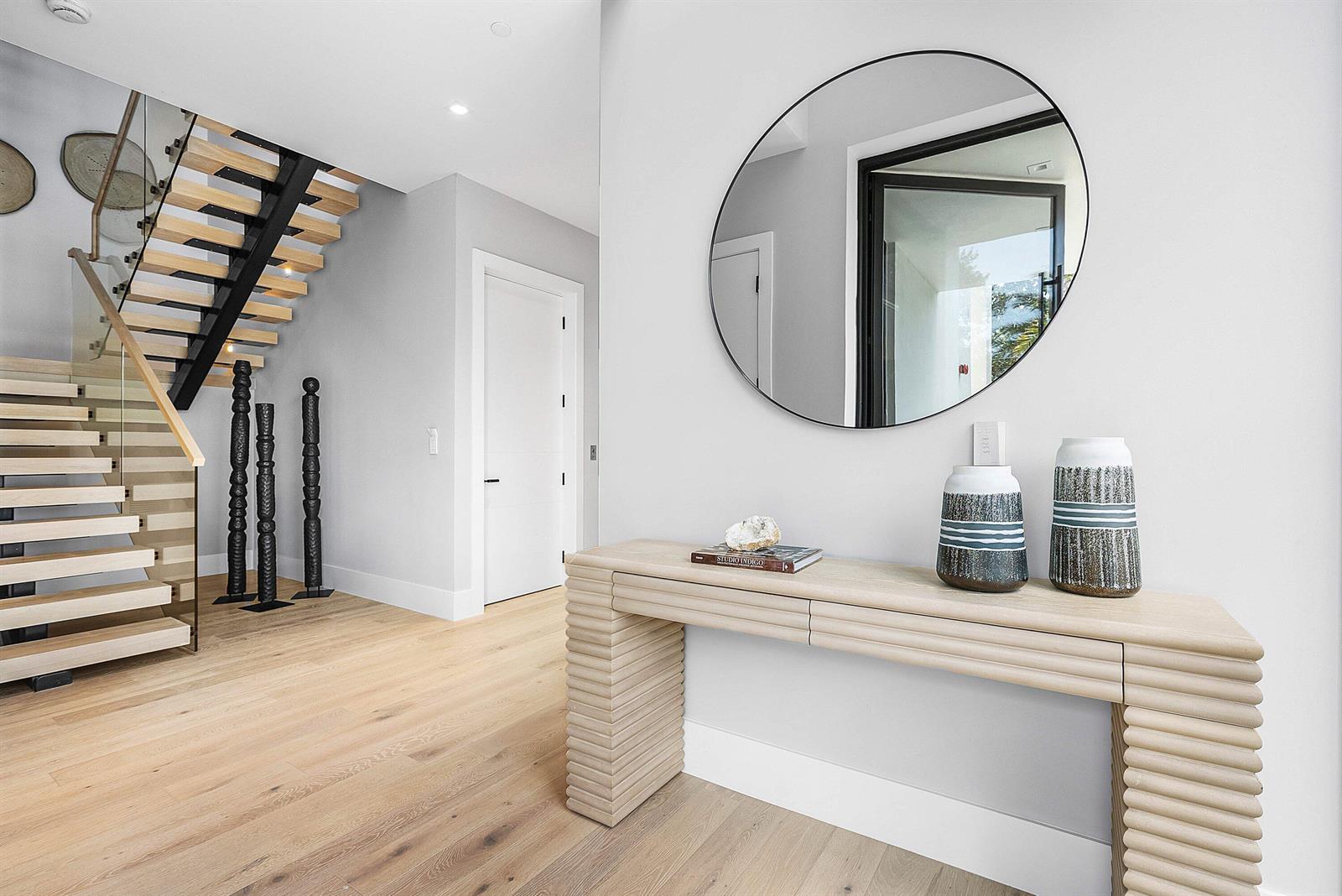 A modern entryway features a light wood console table, a round mirror, and floating stairs — 810 Andrews Avenue, Delray Beach FL 33483, DELRAY BEACH, FL