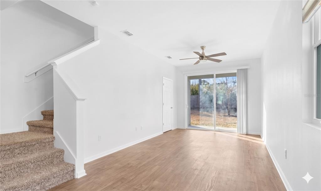 A living room features light wood-look flooring, a carpeted staircase, and sliding glass patio doors — 57 ELMHURST LANE, ST AUGUSTINE, FL