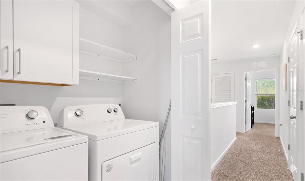 A laundry closet with white appliances and shelving, opening onto a carpeted hallway — 57 ELMHURST LANE, ST AUGUSTINE, FL