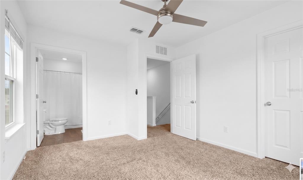 A bedroom with beige carpet, a ceiling fan, an attached bathroom, and two white doors — 57 ELMHURST LANE, ST AUGUSTINE, FL