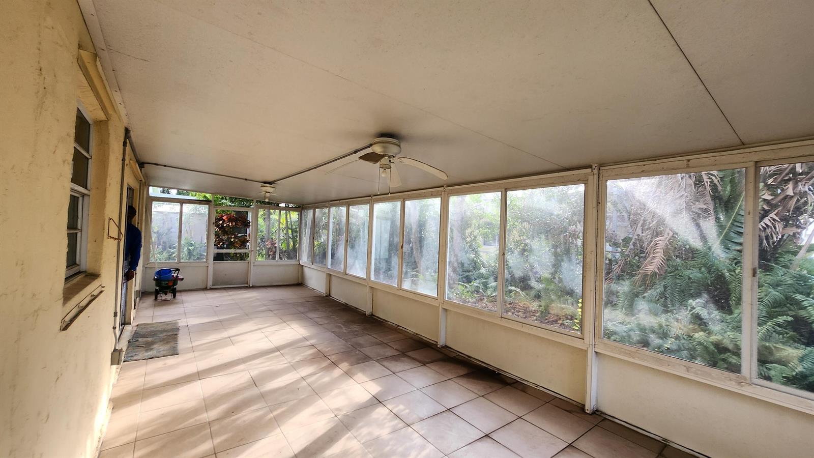 A tiled sunroom features large windows, a ceiling fan, and a view of outdoor greenery — 1207 Hatteras Circle, FL 33413, FL