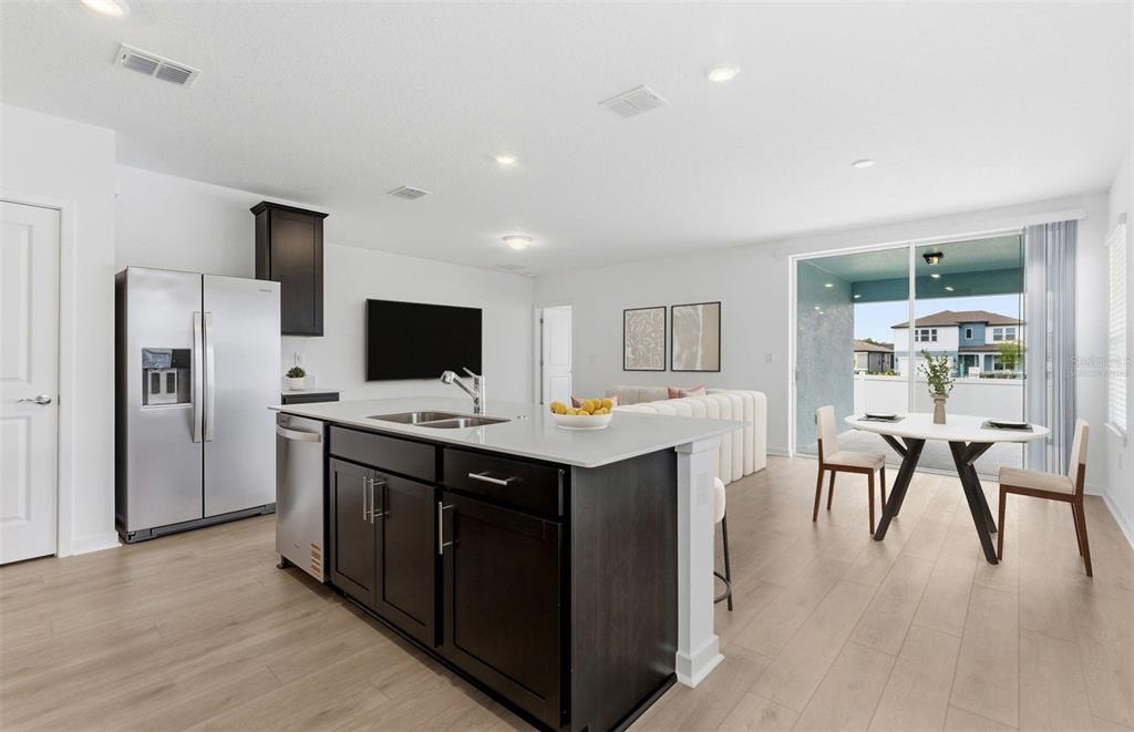 A modern kitchen with a dark island and stainless steel appliances opens to a dining area — 6913 SW 90TH LANE, OCALA, FL