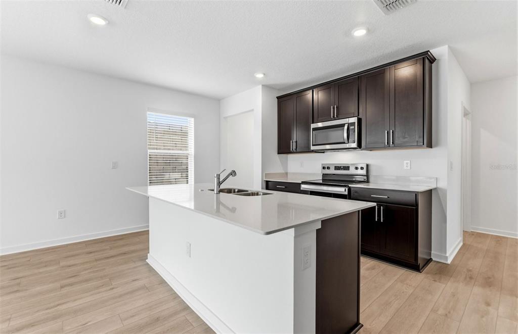 A kitchen with dark cabinets, white countertops, a center island, and light wood-look flooring — 6913 SW 90TH LANE, OCALA, FL