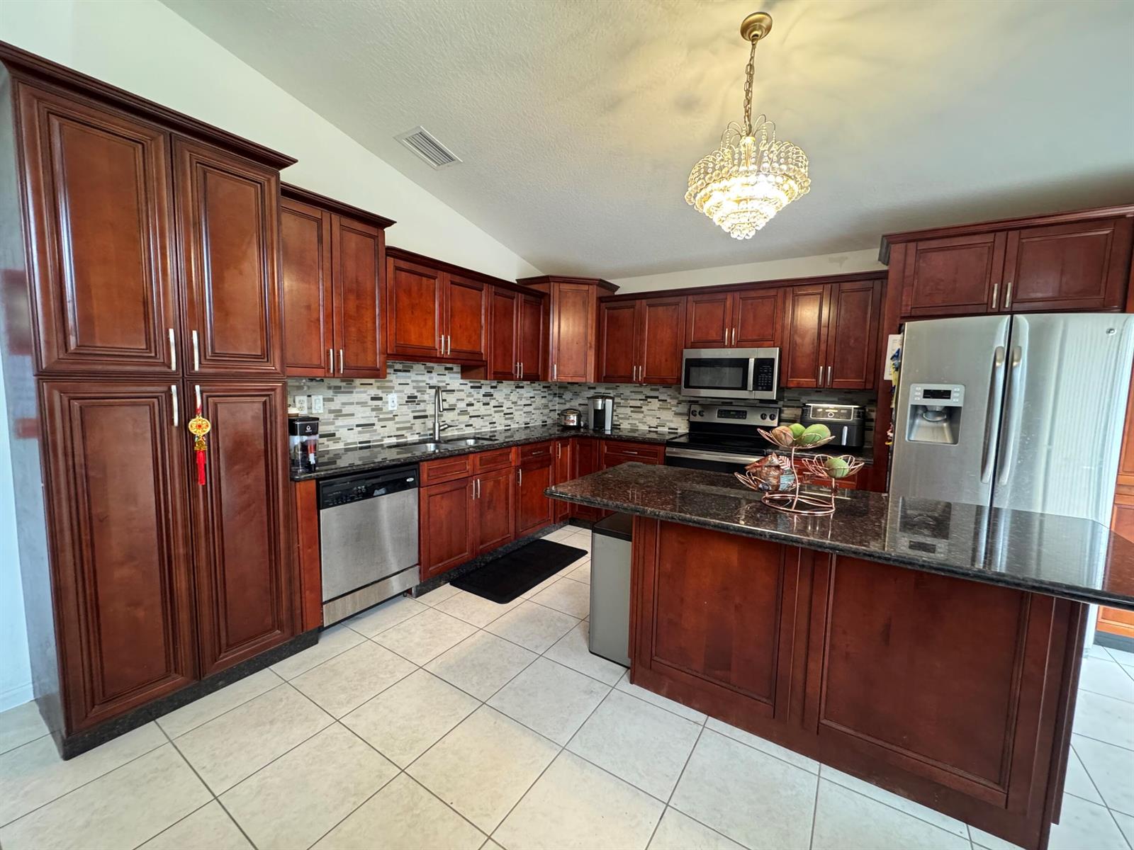 A kitchen features dark wood cabinetry, granite countertops, stainless steel appliances, and a crystal chandelier — 5076 Nautica Lake Circle, FL 33463, FL