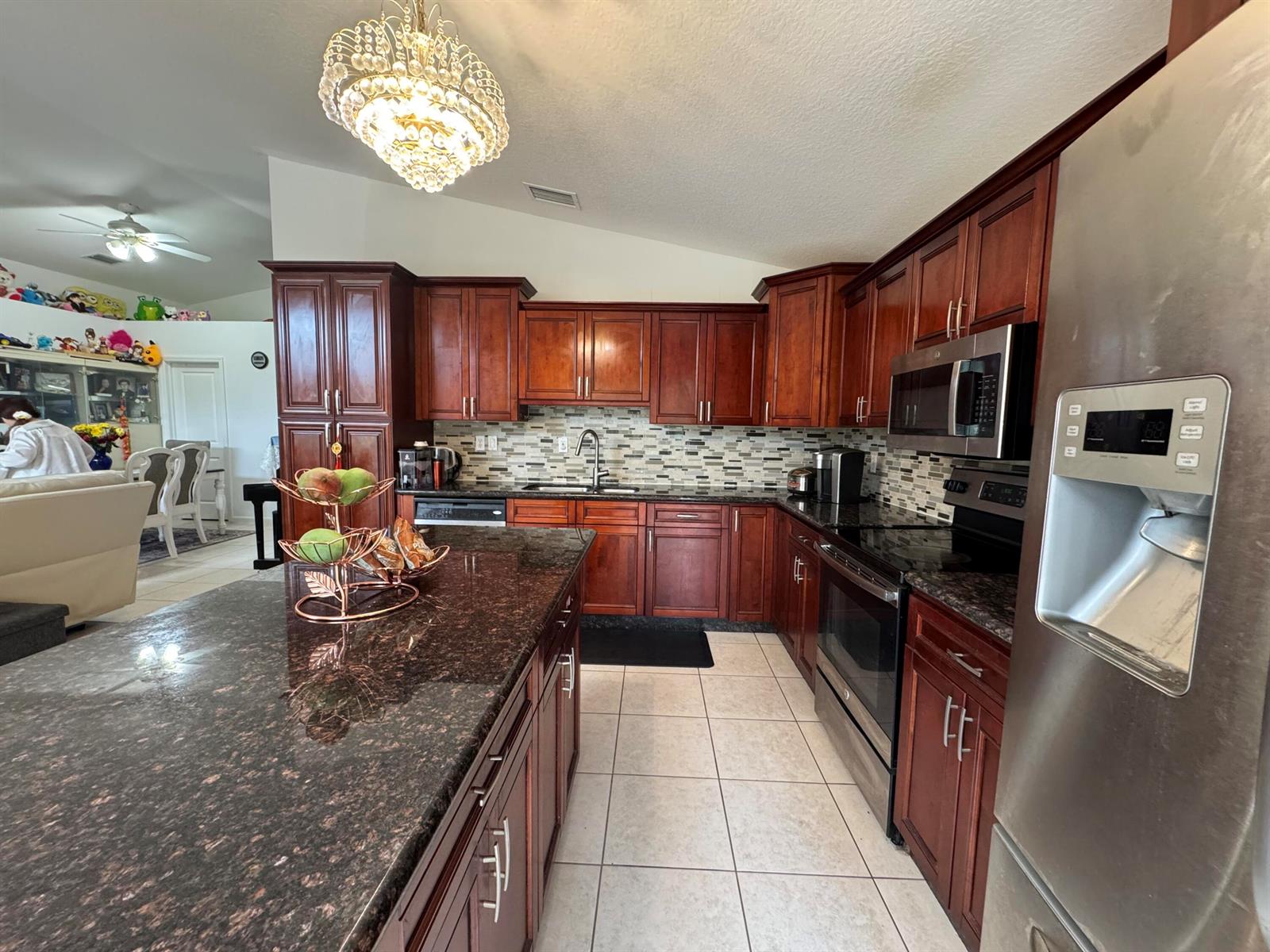 A kitchen features dark wood cabinets, granite countertops, stainless steel appliances, and a chandelier — 5076 Nautica Lake Circle, FL 33463, FL