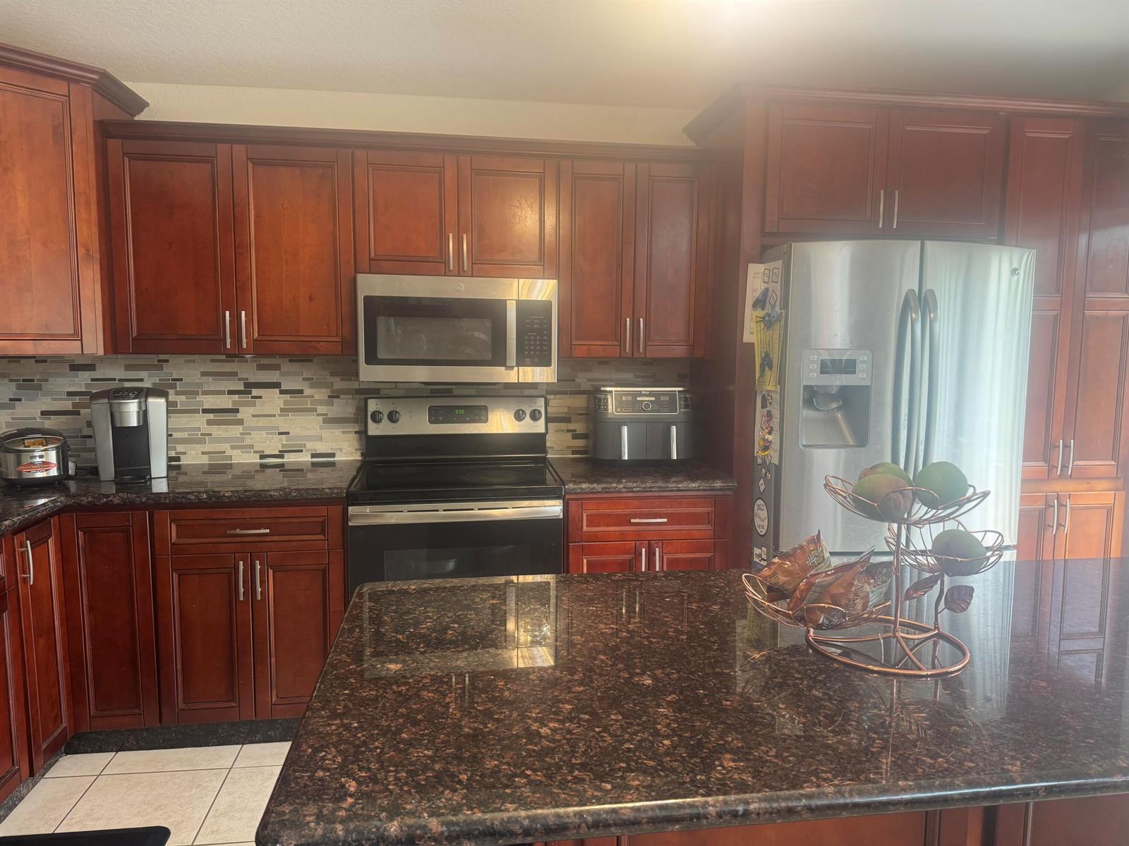 A kitchen features cherry wood cabinets, dark granite countertops, stainless steel appliances, and tile flooring — 5076 Nautica Lake Circle, FL 33463, FL