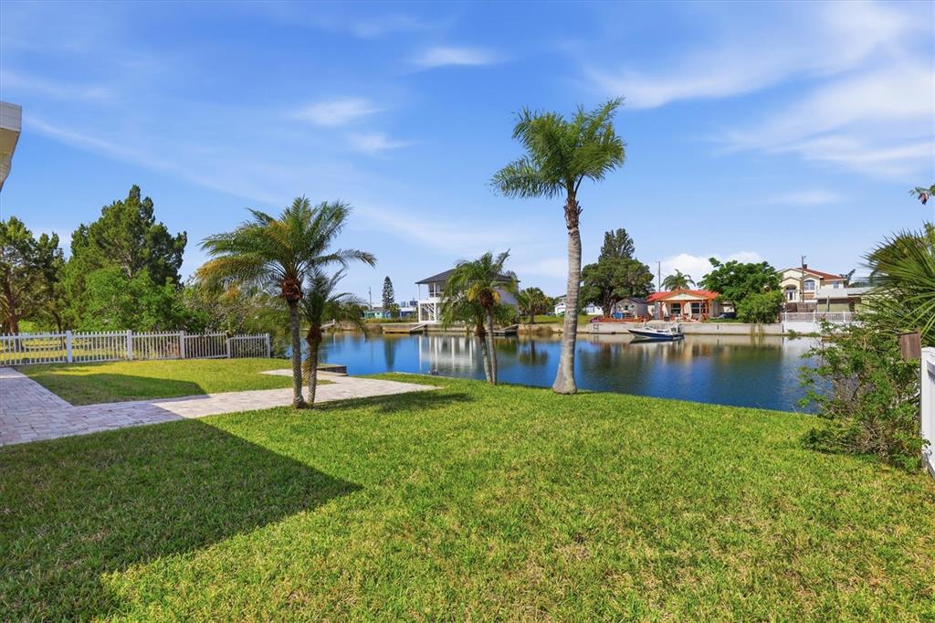 A grassy backyard features palm trees and a stone patio overlooking a canal — 3347 OLEANDER DRIVE, HERNANDO BEACH, FL