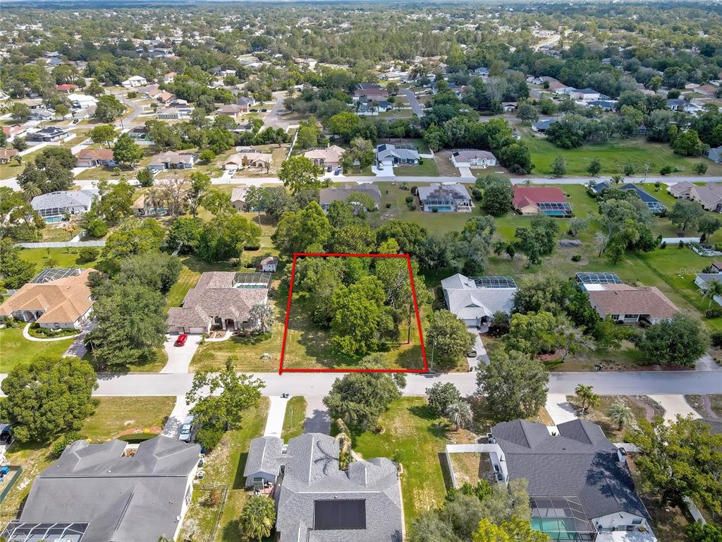 An aerial view shows a vacant, tree-covered residential lot outlined in red between two houses — ORANGEWOOD COURT, SPRING HILL, FL