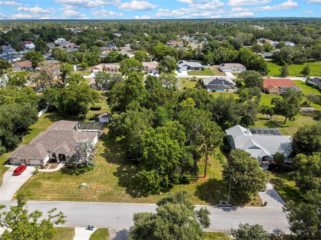 An aerial view shows two suburban houses separated by a large, wooded vacant lot — ORANGEWOOD COURT, SPRING HILL, FL
