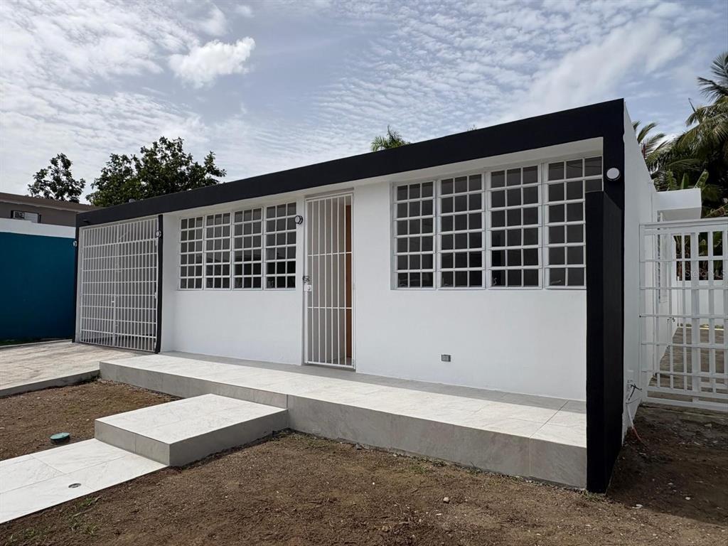 A white, single-story house exterior features a tiled porch, security bars, and black trim — cz8 126A, CAROLINA, PR