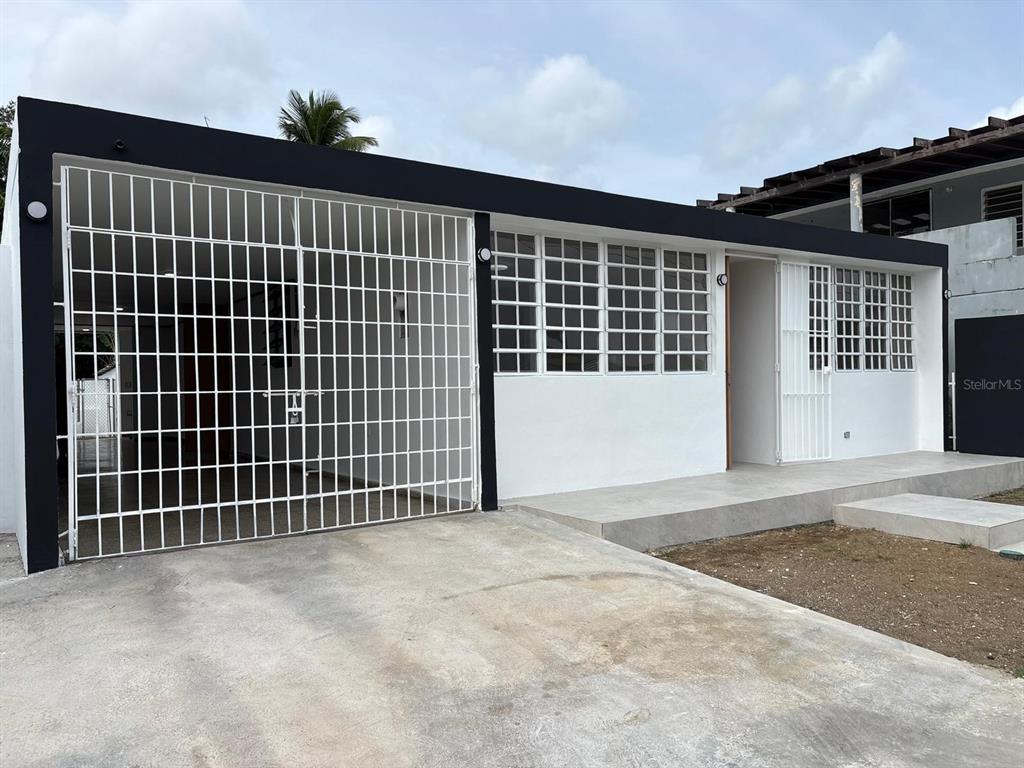 A white house exterior features a black trim, a gated carport, and a concrete porch — cz8 126A, CAROLINA, PR