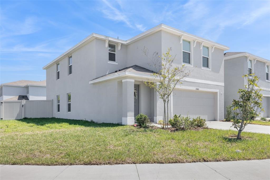 A two-story, light-gray stucco house with a two-car garage and a small front yard — 37092 KINGS CROWN DRIVE, ZEPHYRHILLS, FL