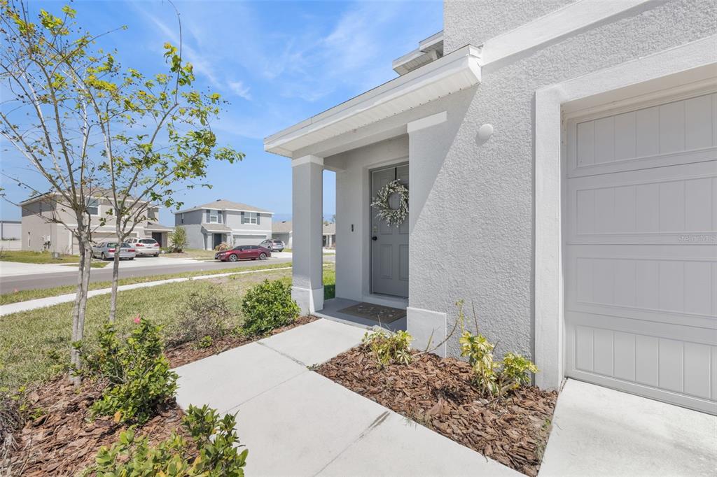 A light gray house exterior features a front door with a wreath and a garage — 37092 KINGS CROWN DRIVE, ZEPHYRHILLS, FL
