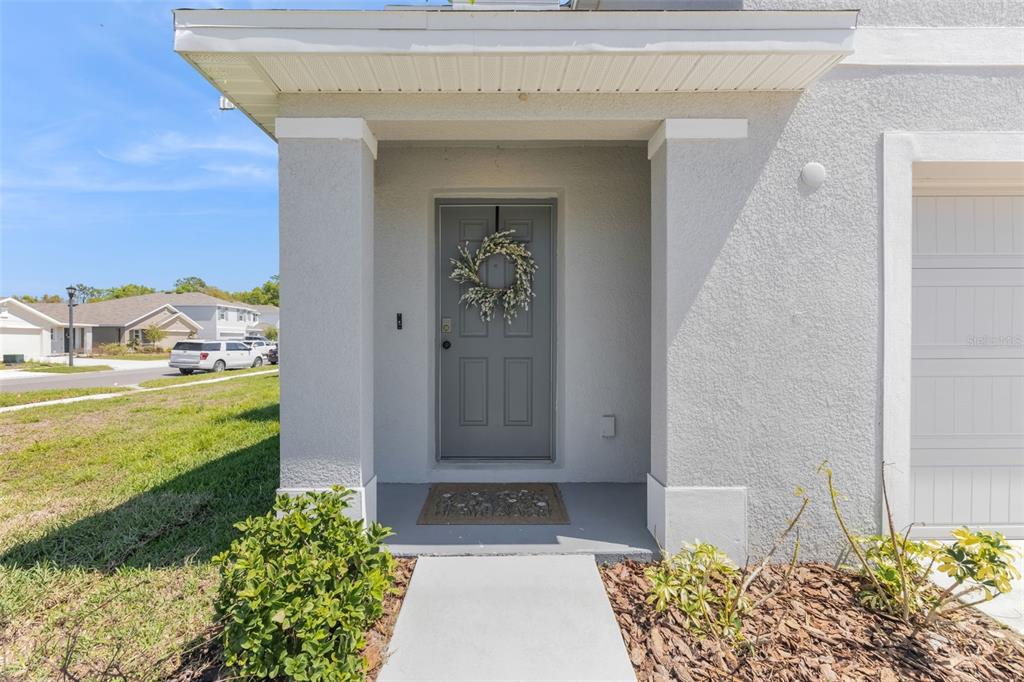 The exterior view shows a gray front door with a wreath under a covered porch — 37092 KINGS CROWN DRIVE, ZEPHYRHILLS, FL