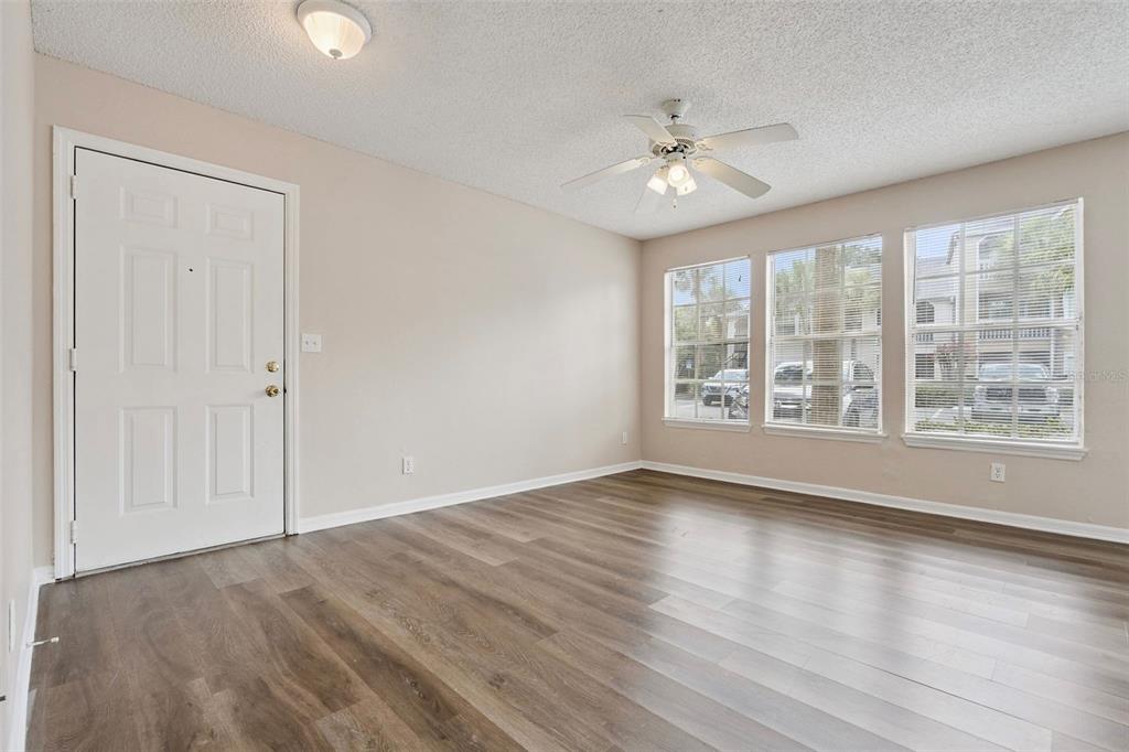 An empty room with light-colored walls, wood-look flooring, a ceiling fan, and three large windows — 1085 S HIAWASSEE ROAD UNIT 513, ORLANDO, FL