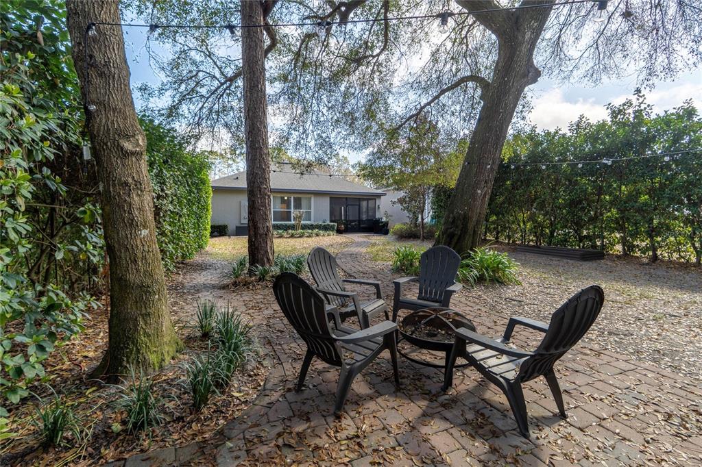 A brick patio with four Adirondack chairs and a fire pit sits under large trees — 184 BIRCHMONT DRIVE, DELAND, FL