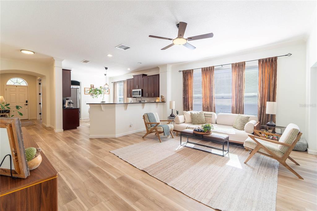 A living room with wood-look flooring, a ceiling fan, and an open kitchen with dark cabinets — 184 BIRCHMONT DRIVE, DELAND, FL
