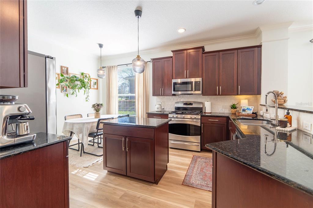 A kitchen with dark wood cabinets, granite countertops, a center island, and an adjacent dining area — 184 BIRCHMONT DRIVE, DELAND, FL