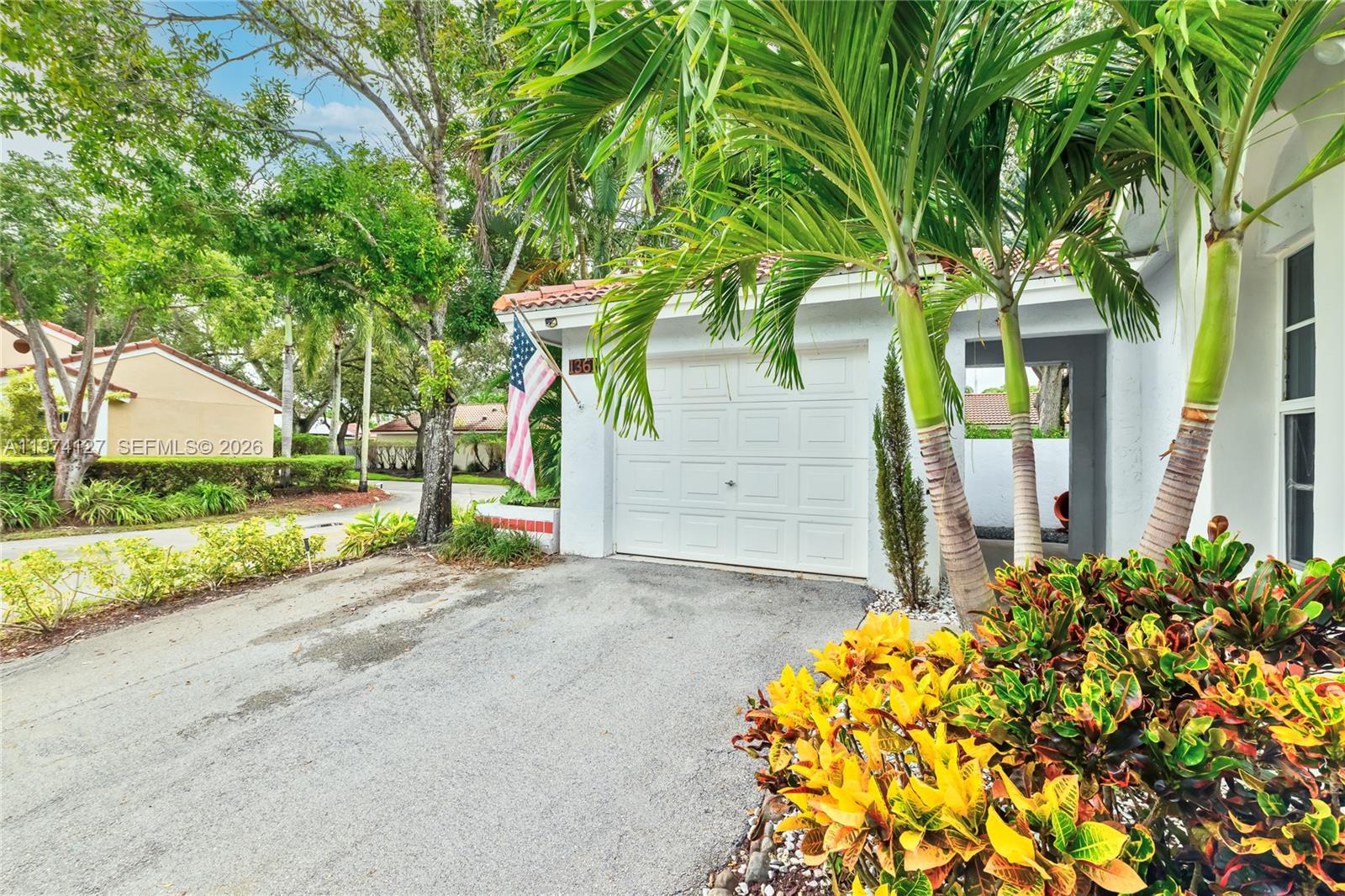 A white garage with a flag and palm trees sits beside a paved driveway — 1361 Seagrape Cir, Weston FL 33326, WESTON, FL