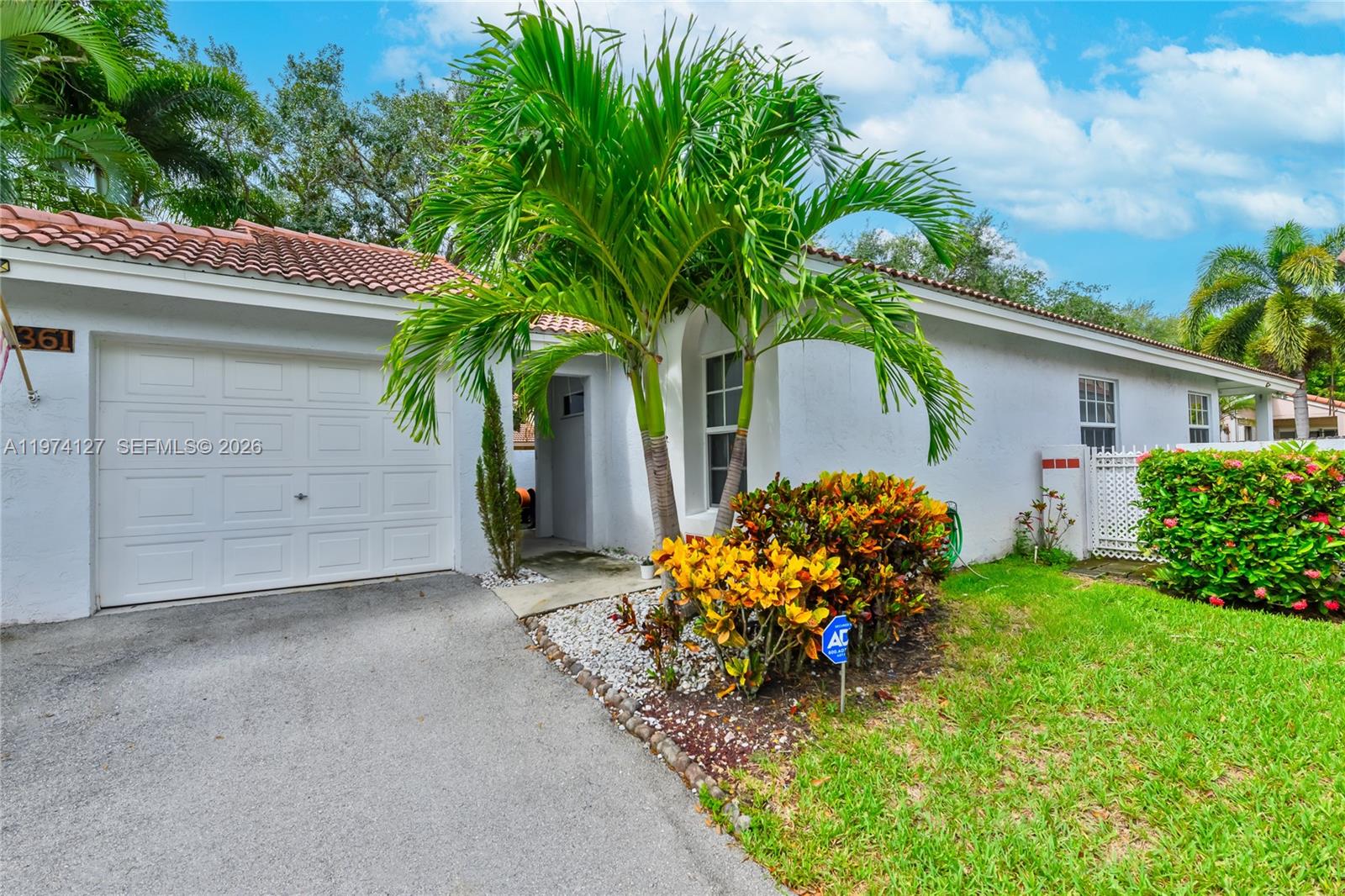A white single-story house features a garage, a palm tree, and a landscaped front yard — 1361 Seagrape Cir, Weston FL 33326, WESTON, FL