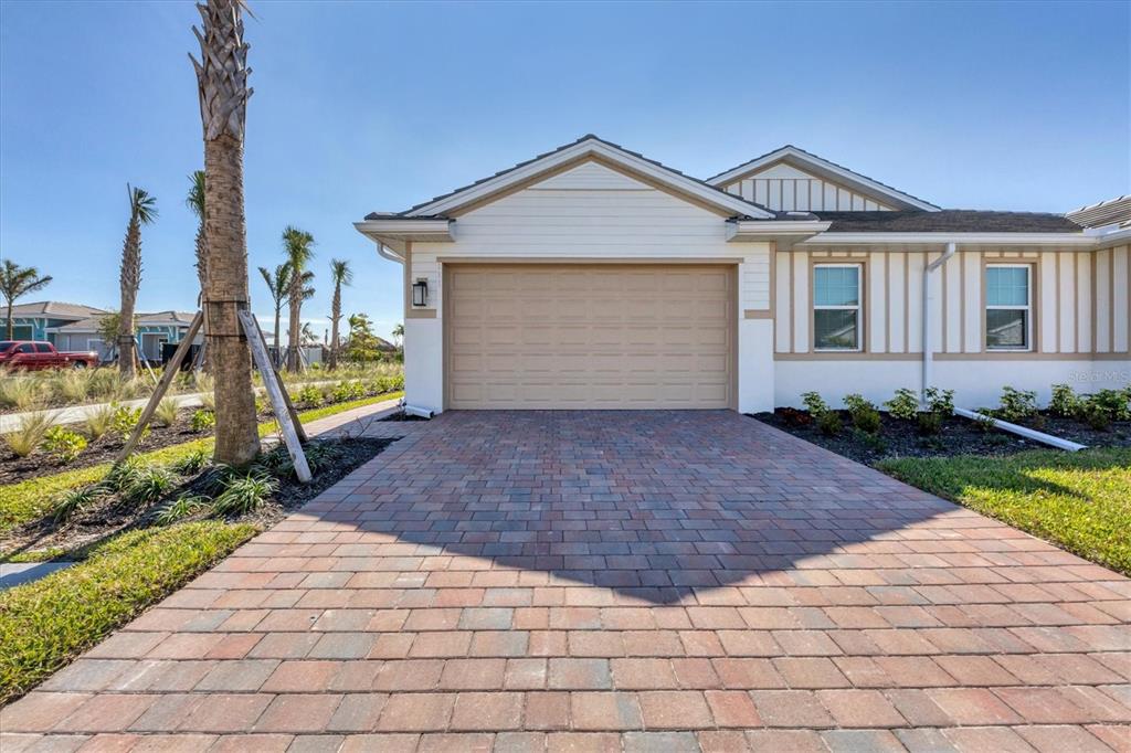 A single-story house exterior with a tan garage door and a brick paver driveway — 111 IBIZA LOOP, VENICE, FL