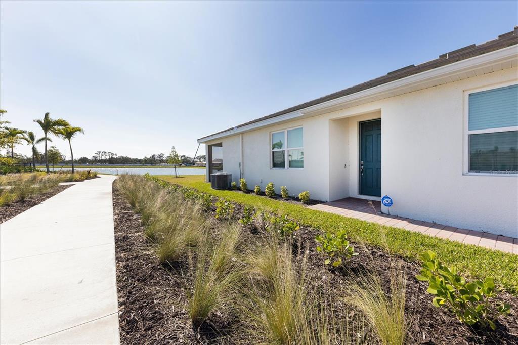 A white house exterior features a dark blue door, a sidewalk, and a nearby pond — 111 IBIZA LOOP, VENICE, FL