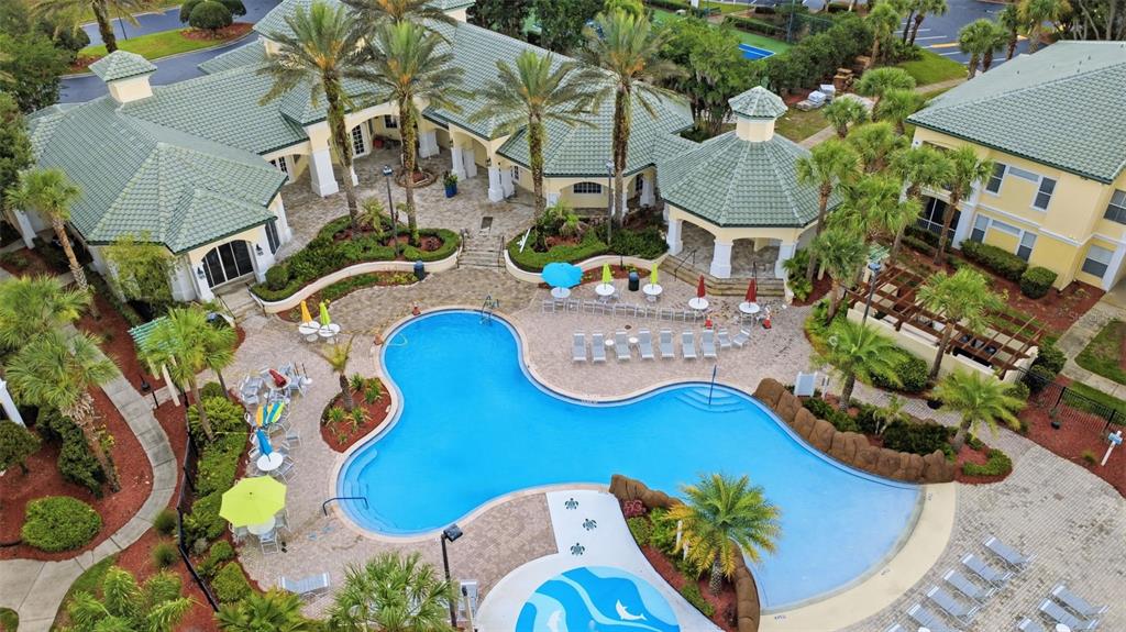 An aerial view shows a resort-style swimming pool surrounded by a patio, palm trees, and buildings — 8807 DUNES COURT UNIT 308, KISSIMMEE, FL