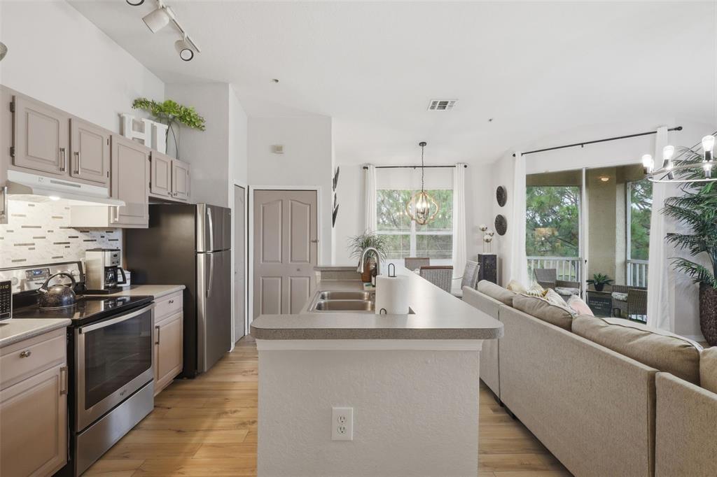 A kitchen with grey cabinets and stainless steel appliances overlooks a living room and balcony — 8807 DUNES COURT UNIT 308, KISSIMMEE, FL