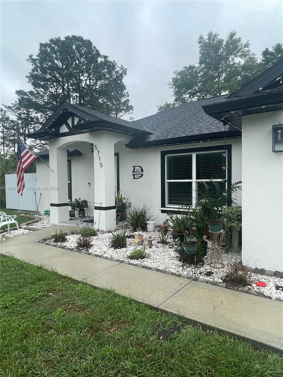 The exterior of a white house features a covered entryway, black trim, and landscaping — 5715 SW 128TH Pl, Ocala FL 34473, OCALA, FL