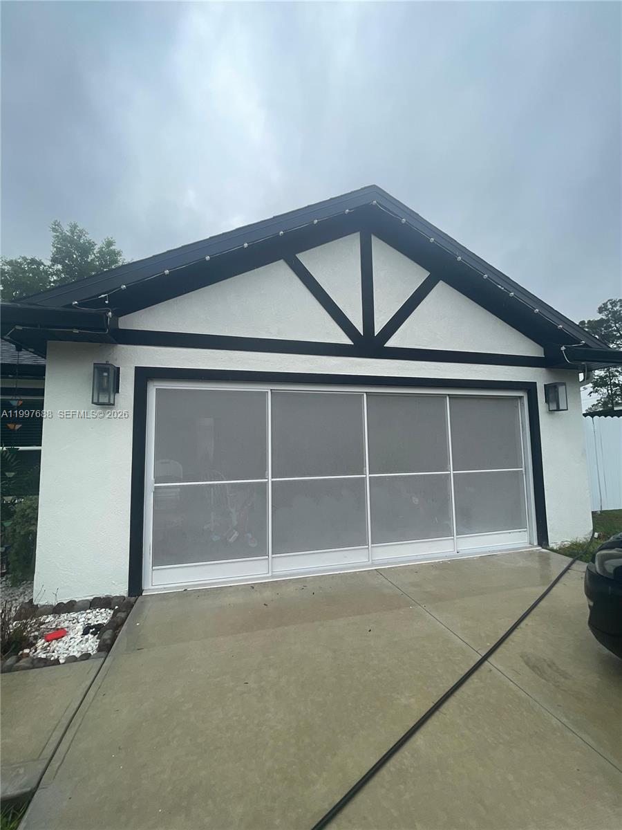 A white house exterior features a garage with a sliding screen door and dark trim — 5715 SW 128TH Pl, Ocala FL 34473, OCALA, FL
