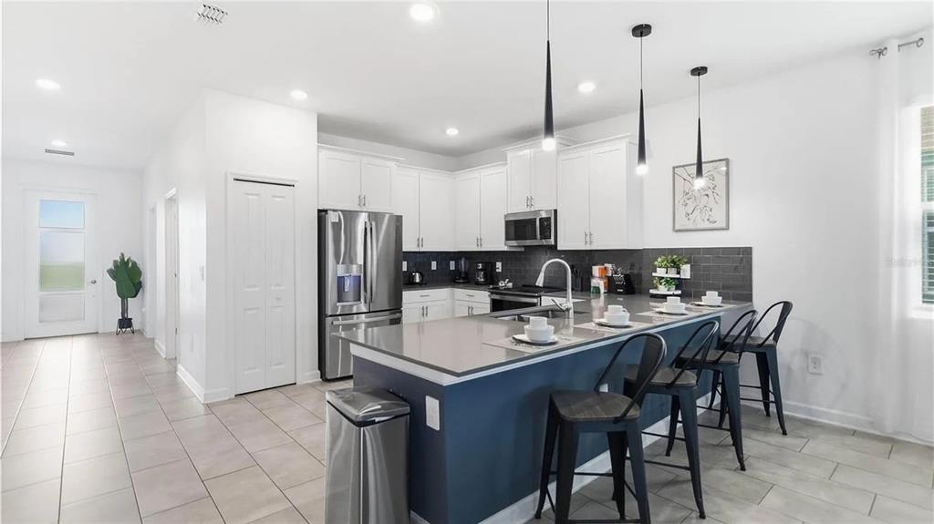 A modern kitchen features white cabinets, a dark blue island with bar seating, and gray tile — 9114 SOMMERSET HILLS DRIVE, DAVENPORT, FL