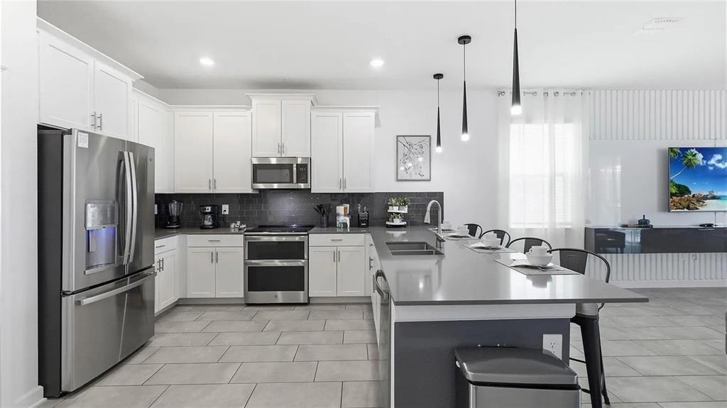 A modern kitchen features white cabinetry, stainless steel appliances, a gray island, and tile flooring — 9114 SOMMERSET HILLS DRIVE, DAVENPORT, FL