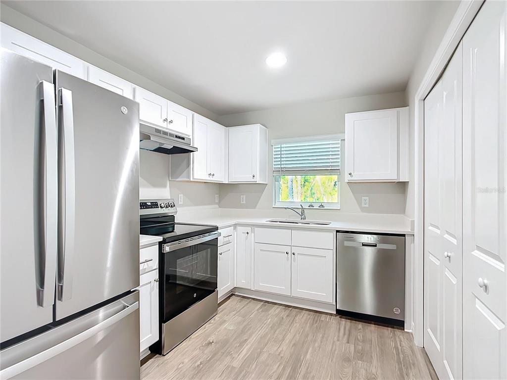 A kitchen features white cabinets, stainless steel appliances, and light wood-look flooring — 9474 N CAMEL DRIVE, DUNNELLON, FL
