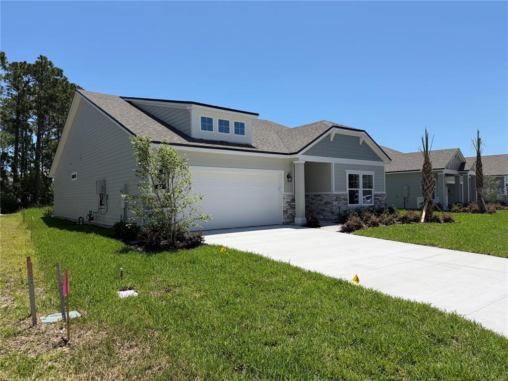 A single-story house with a two-car garage, light siding, stone accents, and a concrete driveway — 32 PERSEUS AVENUE, FLAGLER BEACH, FL